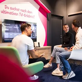 Drei Personen sitzen in modernem Raum und testen interaktives TV-Erlebnis mit Smart-TV.
