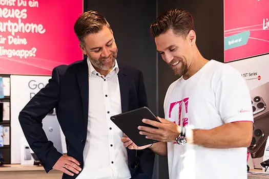 Telekom Mitarbeiter berät Kunden im Shop mit Tablet und Smartphone-Angebot